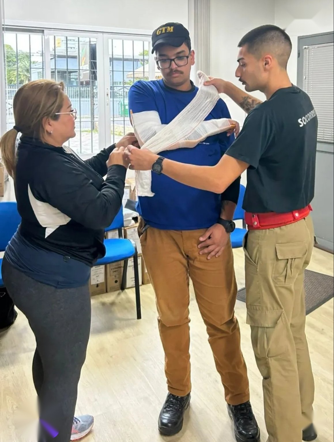 Fernando Wolff ensinando a aplicar bandagem em um aluno, com outra aluna ajudando